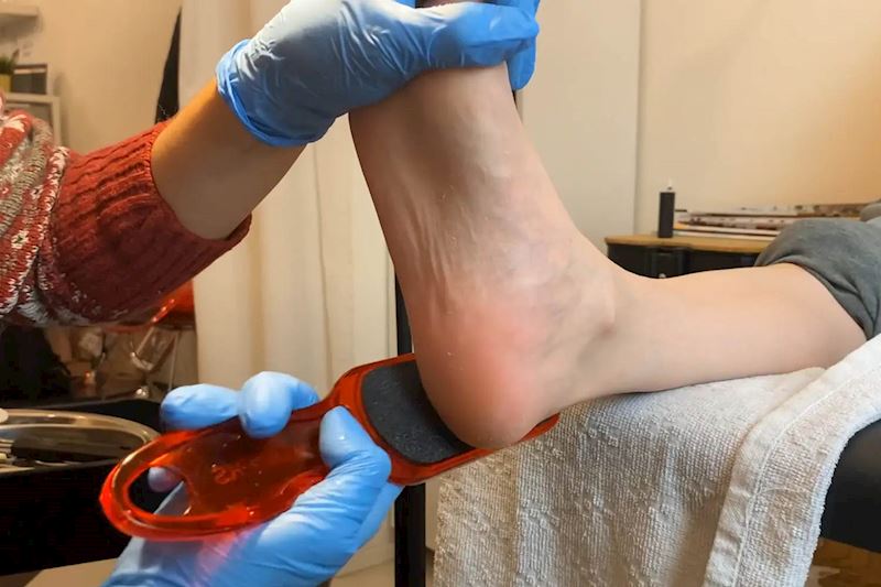 Pedikérka pomocí pilníku odstraňuje odumřelou kůži na noze